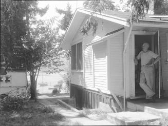 Untitled (side of house with man in doorway, overlooking lake)