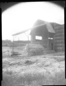 Untitled (barn with awning and haystacks)